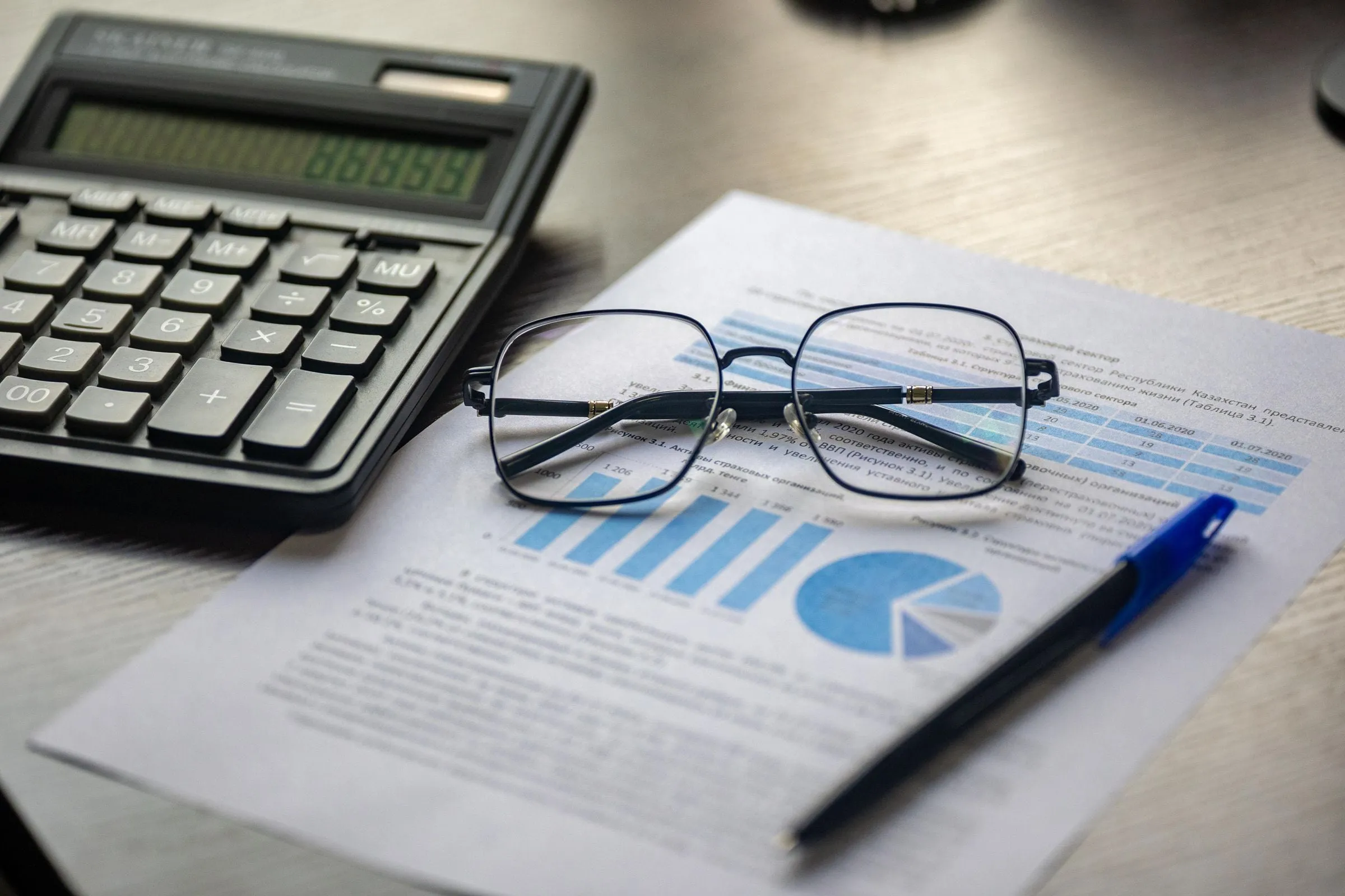 Relatório financeiro com gráficos azuis, calculadora, caneta e óculos sobre a mesa